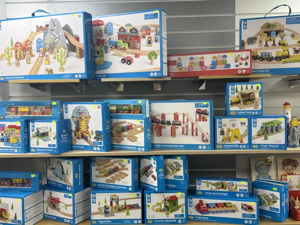 Colorful wooden train sets and accessories displayed on shelves, featuring various themes like safari and western.