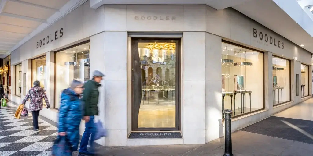 Elegant storefront of Boodles jewelry, showcasing luxurious window displays, with pedestrians walking on a patterned sidewalk nearby.
