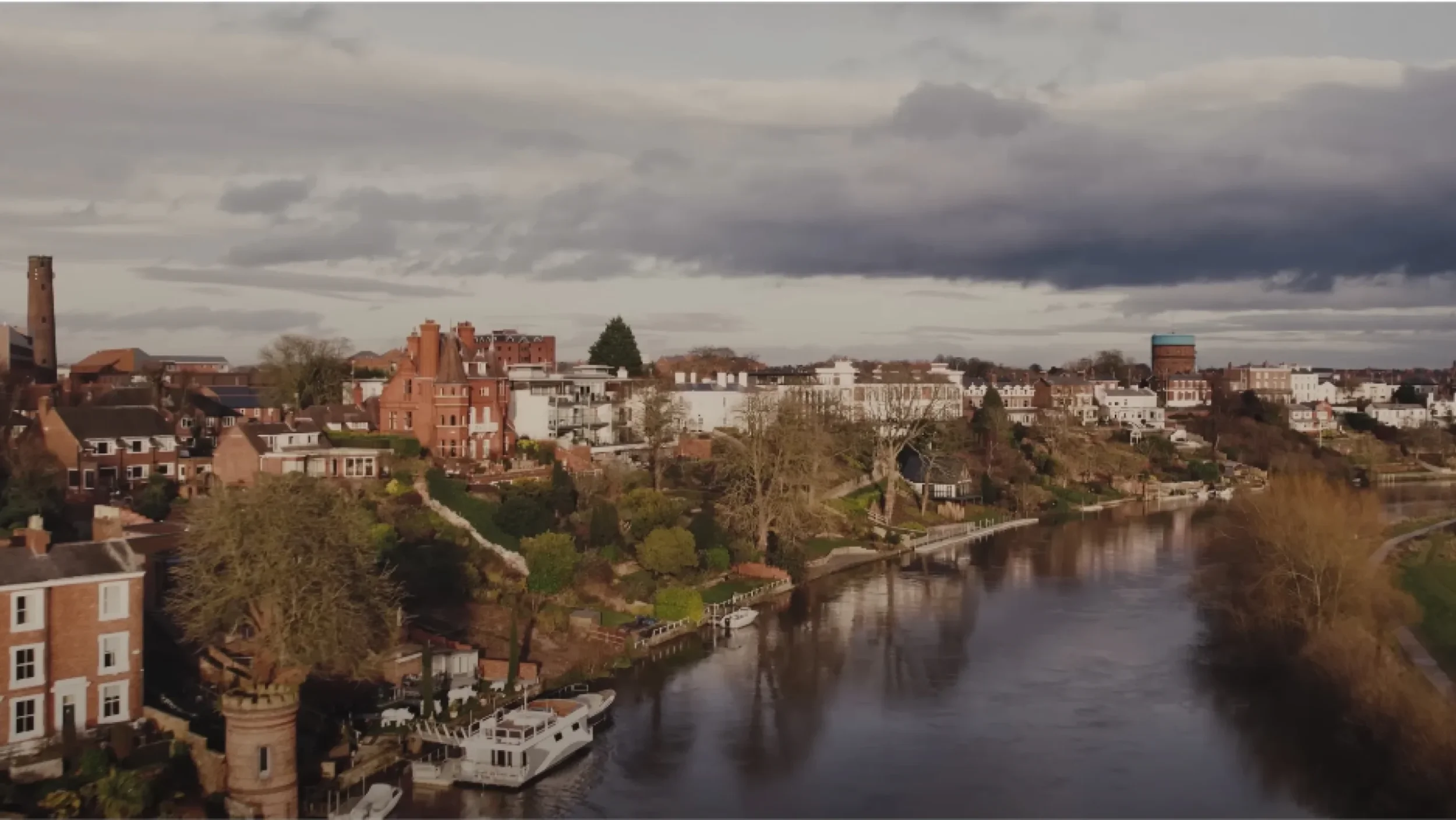 Aerial view of the River Dee winding through Chester with historic buildings under a cloudy sky.