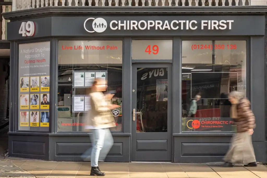 A modern chiropractic clinic storefront displaying services for optimal health and pain relief, with a busy street and pedestrians in motion.