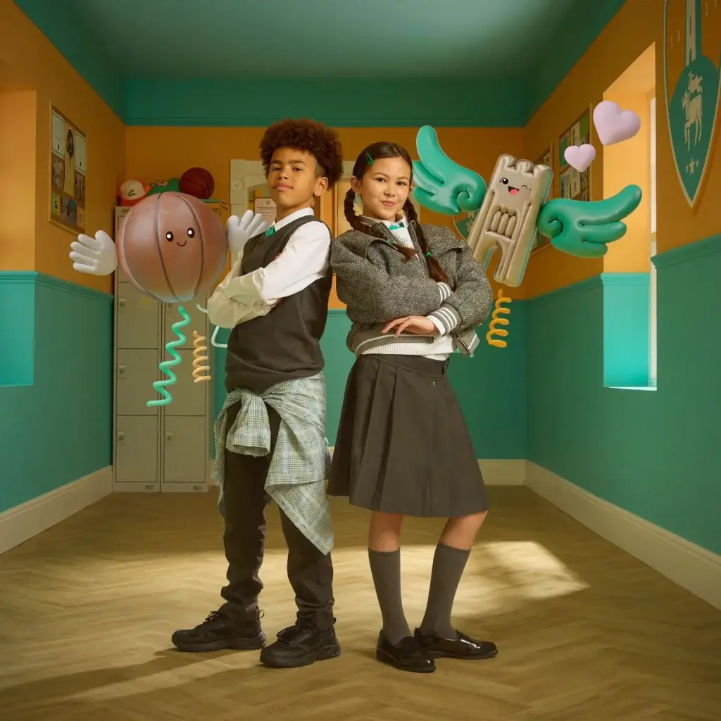 A young boy and young girl pose in school uniform in front of a colourful background