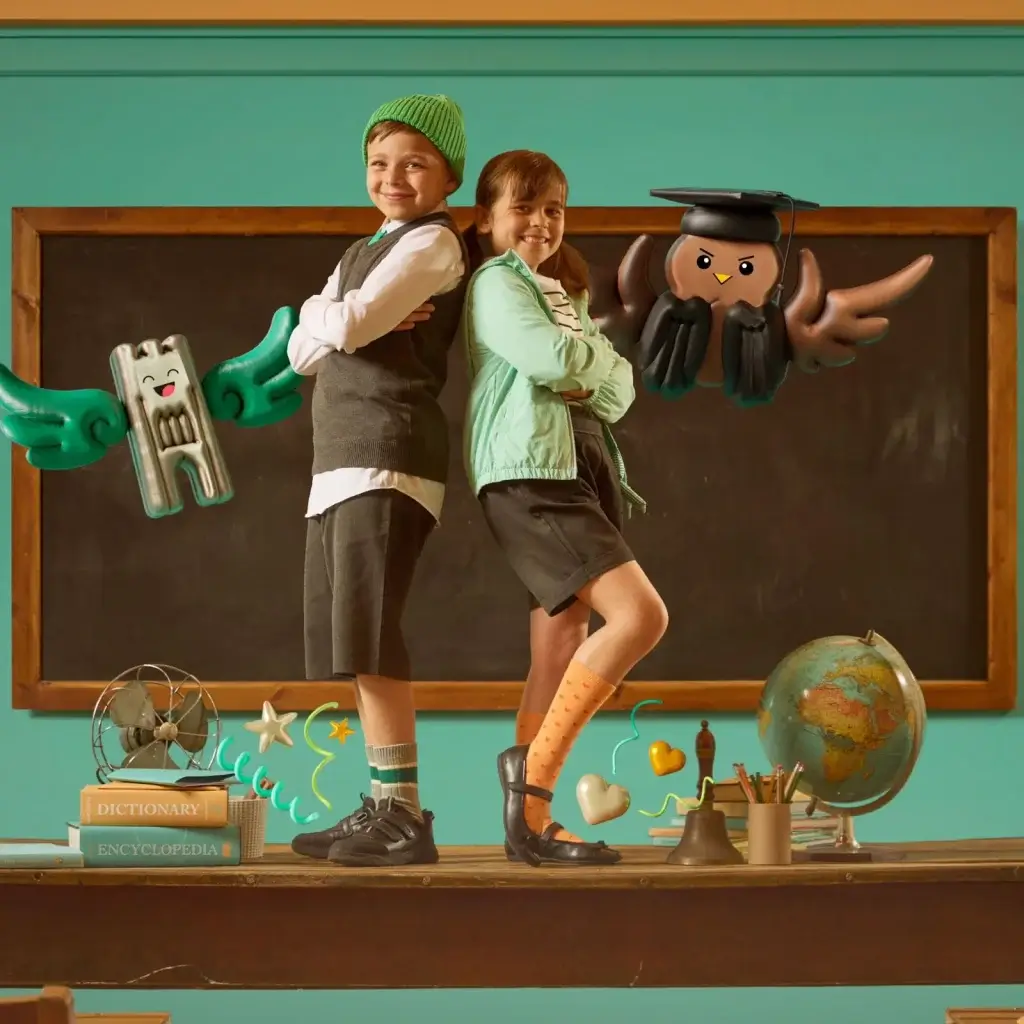 A young boy and young girl pose on a school desk in uniform infant of a chalk board