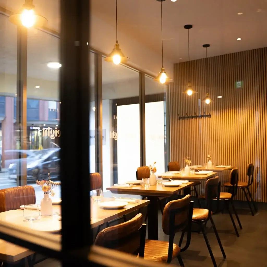 Modern restaurant interior featuring wooden tables, stylish chairs, and warm pendant lighting, creating an inviting atmosphere.