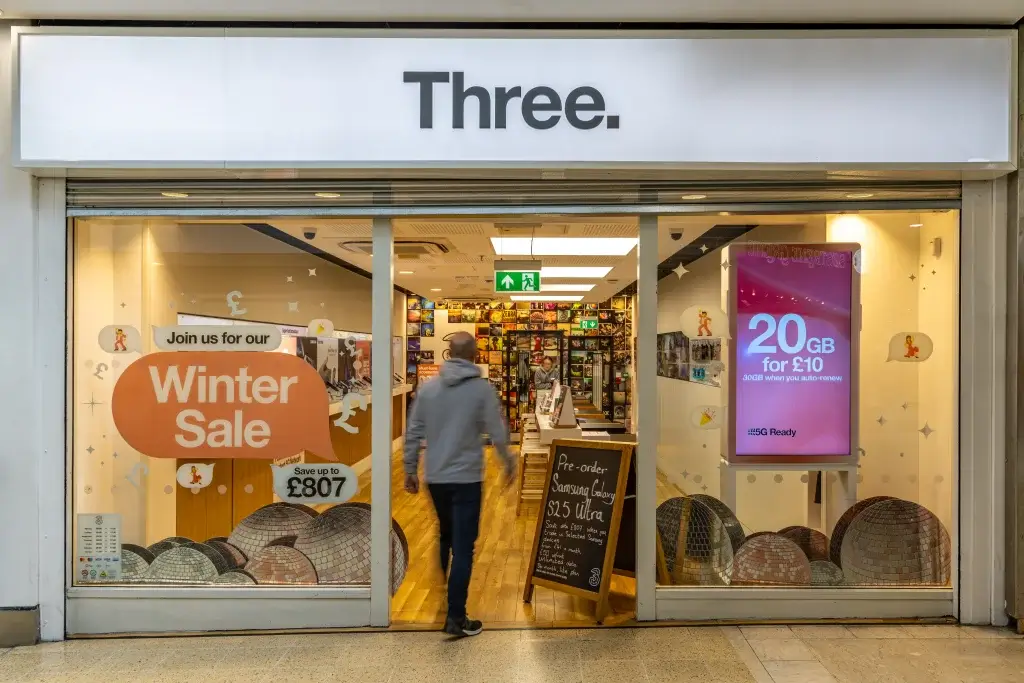 A customer enters a Three mobile network store featuring a "Winter Sale" sign and promotional offers displayed prominently in windows.