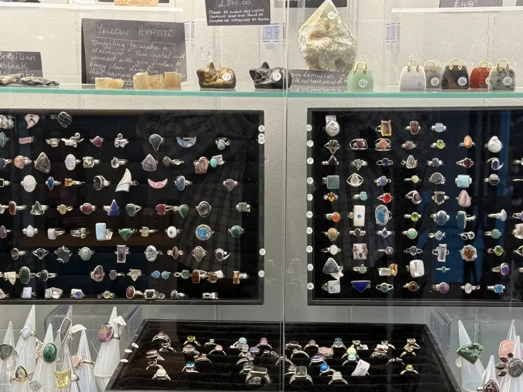 A display case filled with various rings featuring colorful gemstones, with signs describing crystal properties like Yellow Apatite.