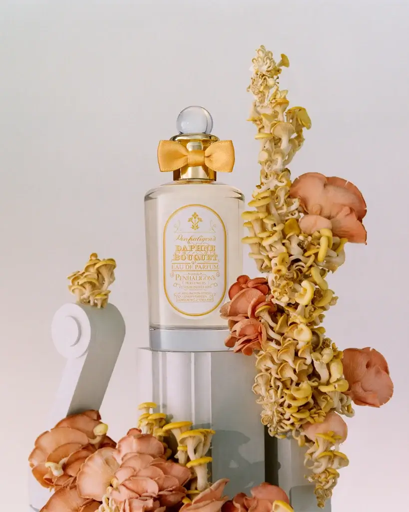 A stylish bottle of perfume adorned with a bow, surrounded by organic, colorful mushrooms against a soft backdrop.