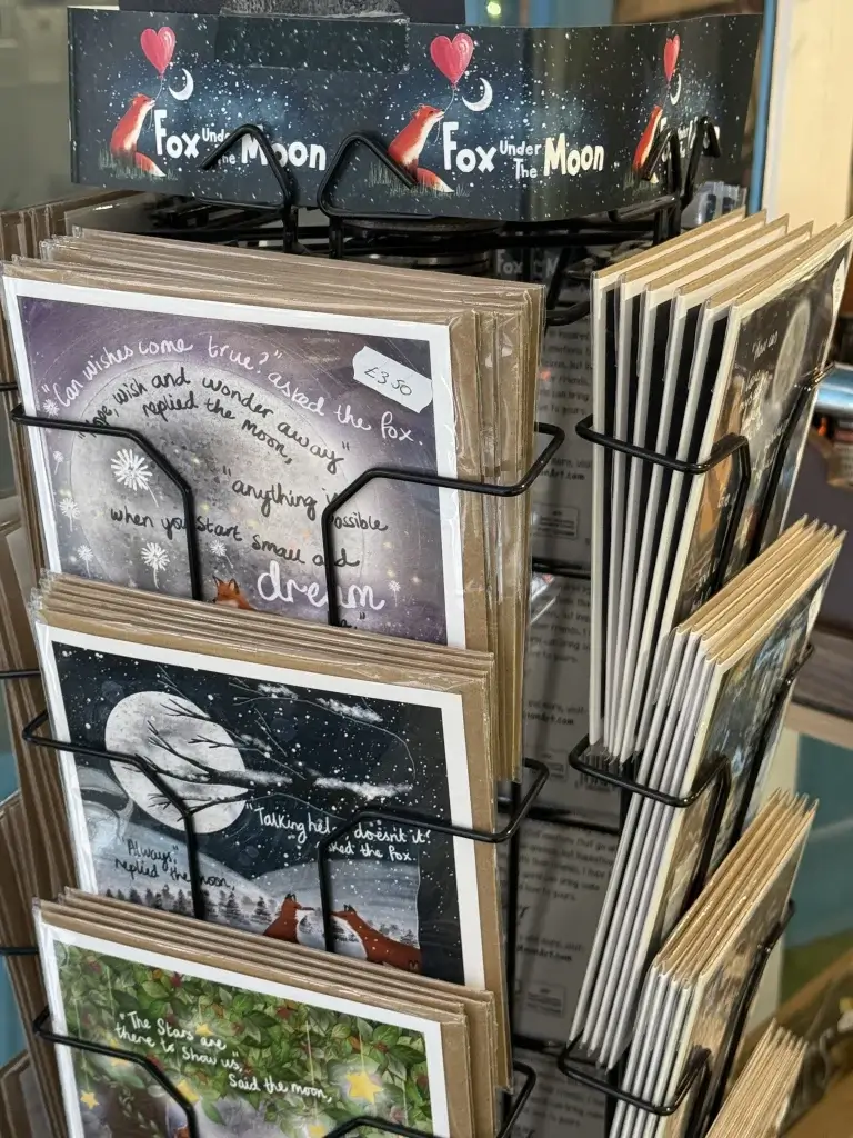 Display rack filled with illustrated greeting cards featuring whimsical fox and moon themes, titled "Fox Under the Moon." Price tag visible.