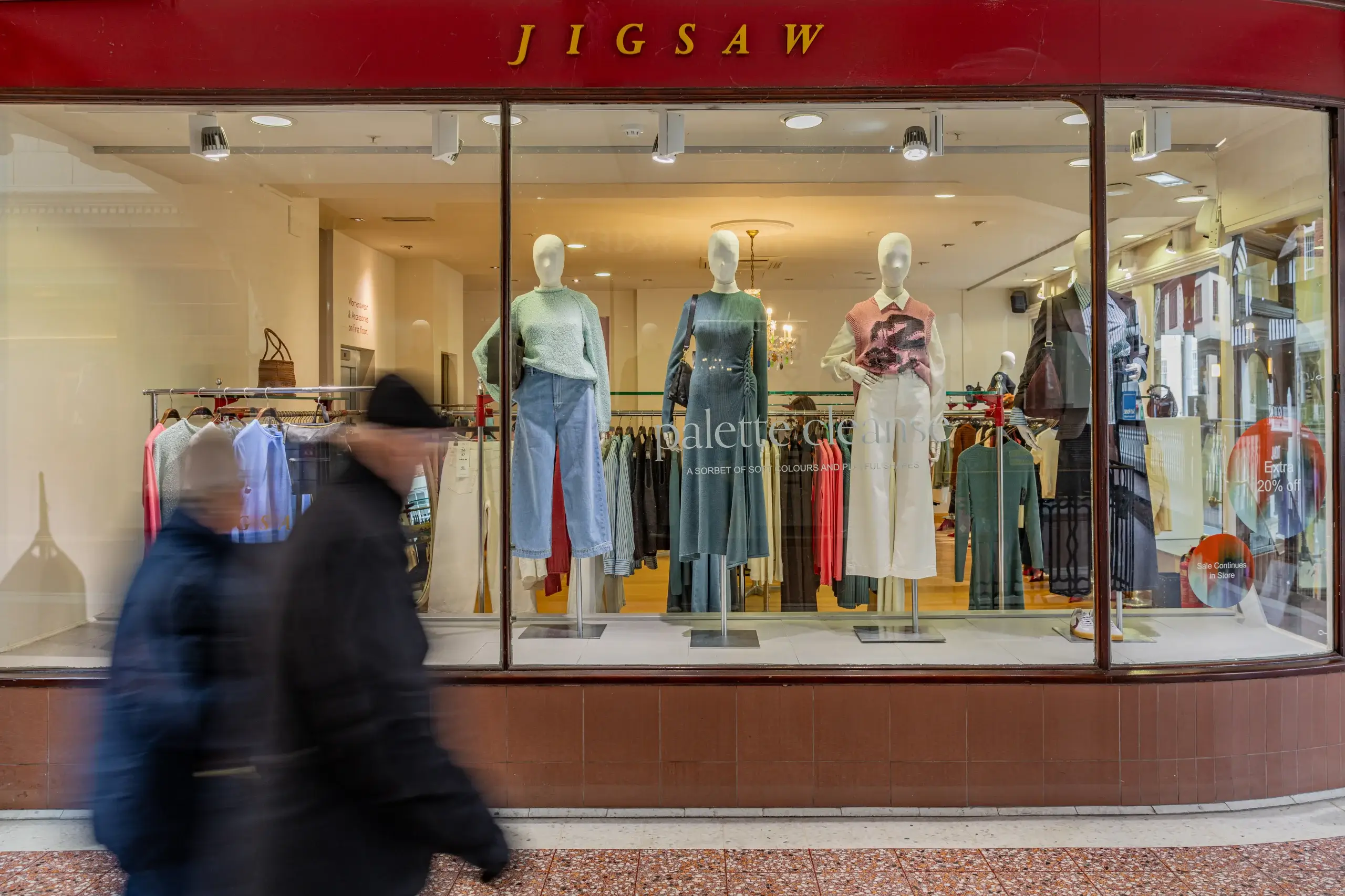 Display window of a Jigsaw store featuring various stylish clothing items on mannequins, with passersby in motion outside.