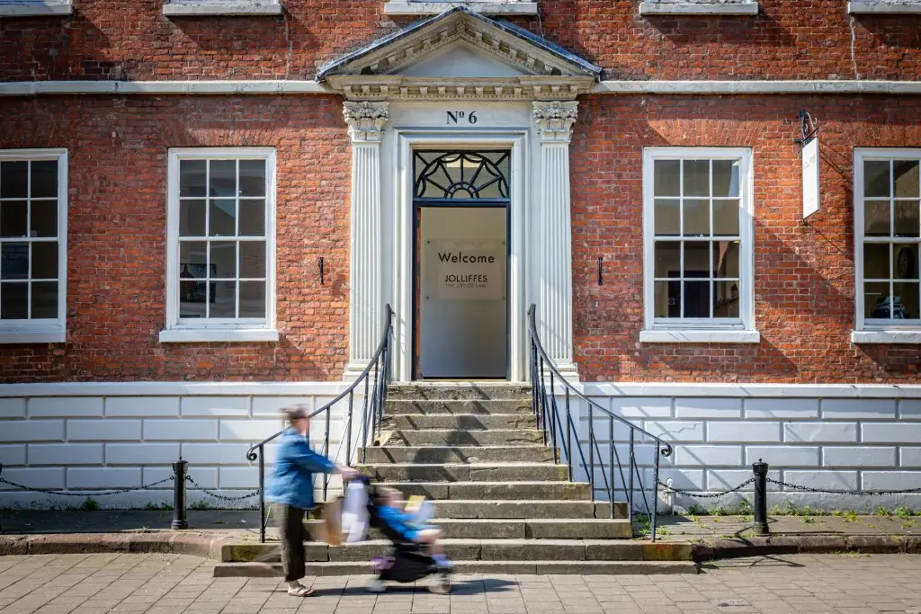 A person walks past a historic brick building with an inviting entrance and decorative iron railings.