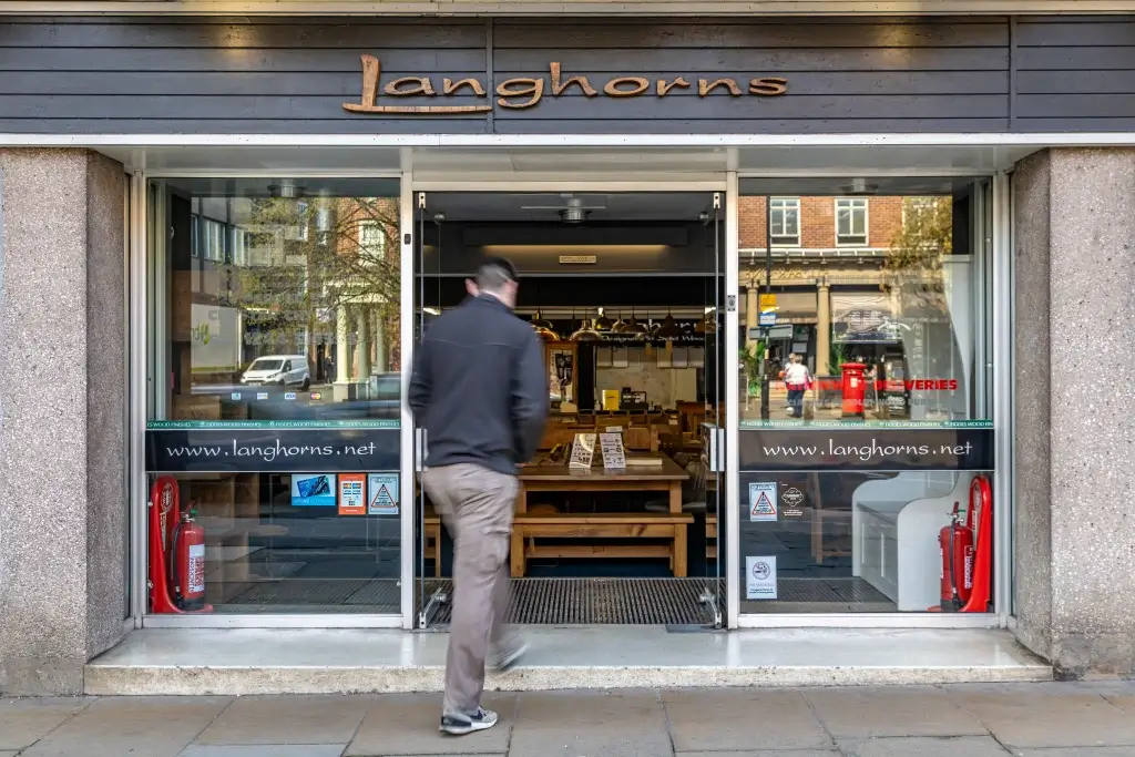 A person enters Langhorns, a cozy eatery with wooden tables and a welcoming interior, located at street level.