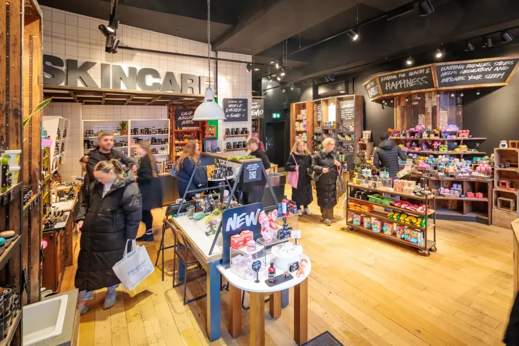 Busy skincare shop interior with wooden shelving, large SKINCARE sign, tables of products and shoppers.