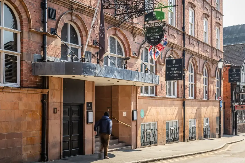 View of the New Blossoms Hotel entrance with a blurred figure walking up the stairs; flags and signs adorn the brick facade.