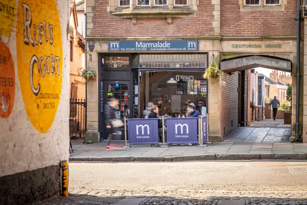 A cozy café, Marmalade, with outdoor seating, located on a charming street adorned with historic brick buildings.
