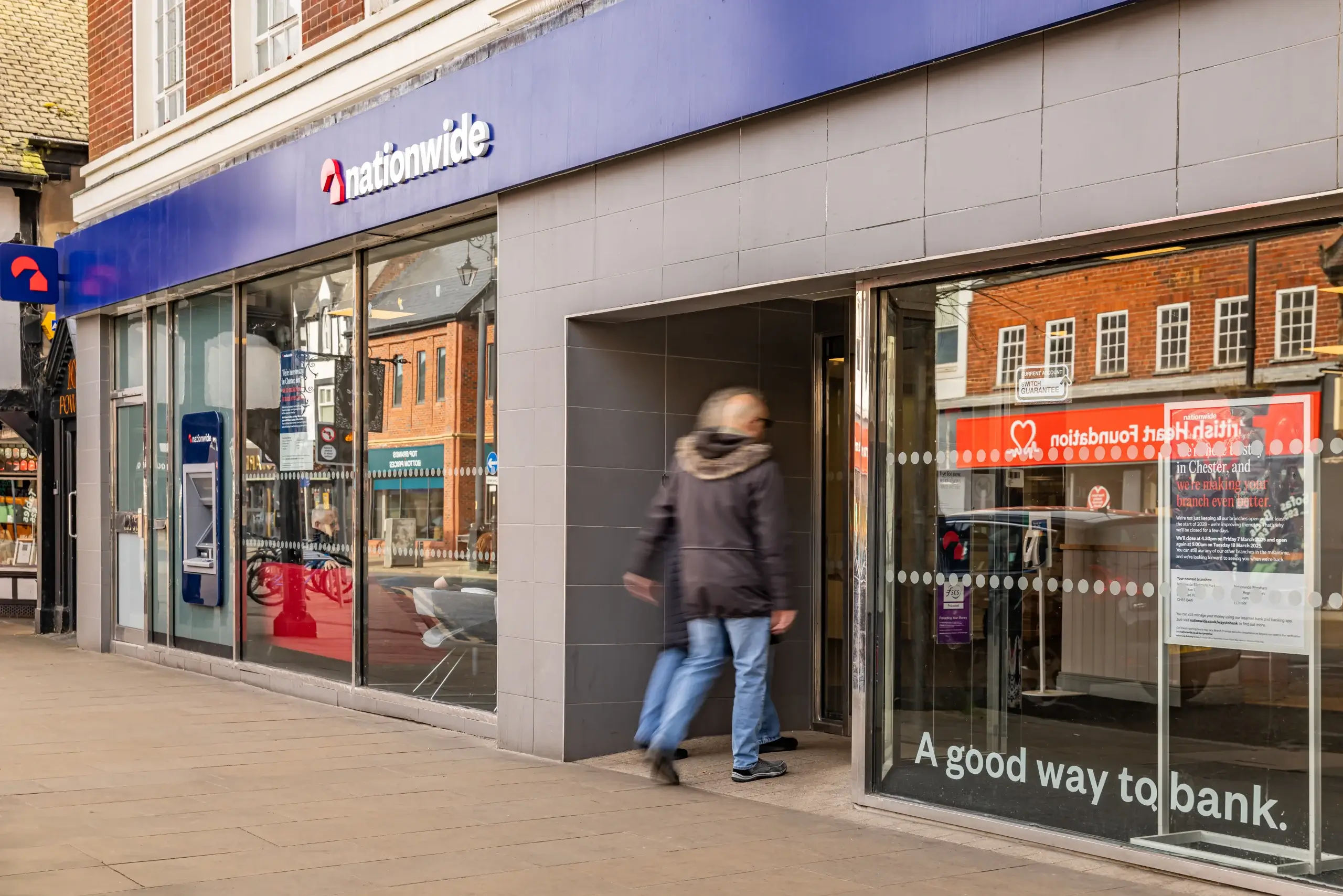 A person walks into a Nationwide bank branch with large glass windows displaying the slogan "A good way to bank."