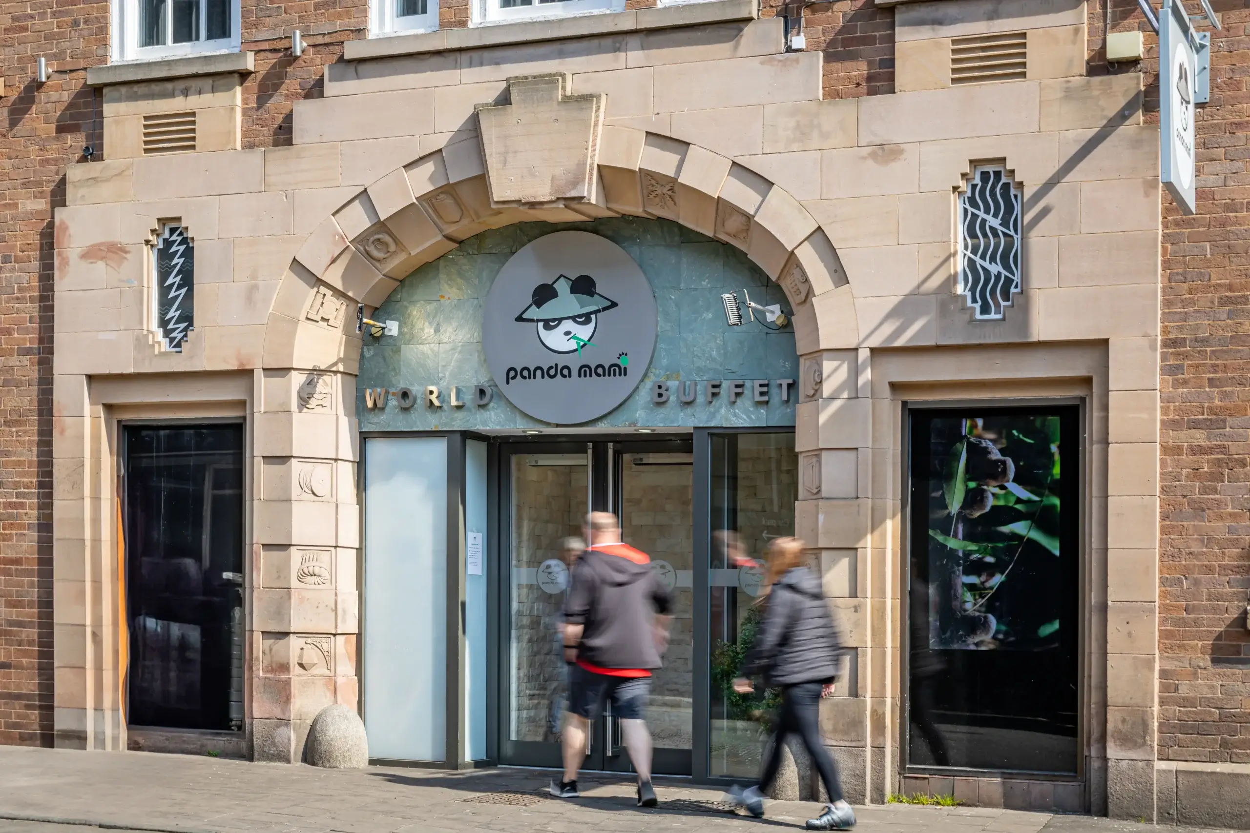 Entrance of Panda Mami World Buffet with a whimsical panda logo on the sign; people walking in and out on a sunny day.