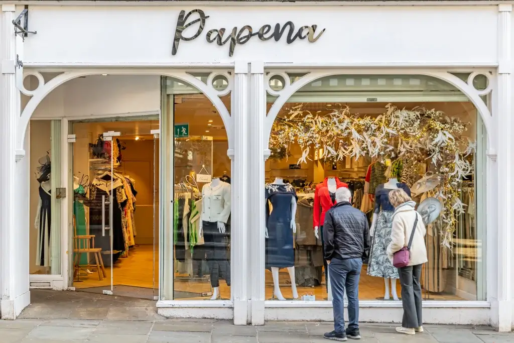 A boutique window displays stylish clothing items, adorned with decorative flowers, inviting passersby to explore the fashion offerings.
