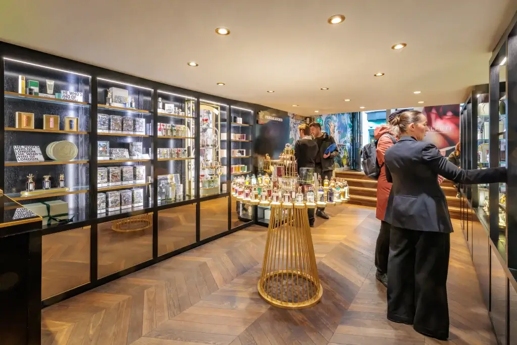 Perfume boutique interior with backlit wall displays, a central round stand of perfume bottles and shoppers browsing the selection