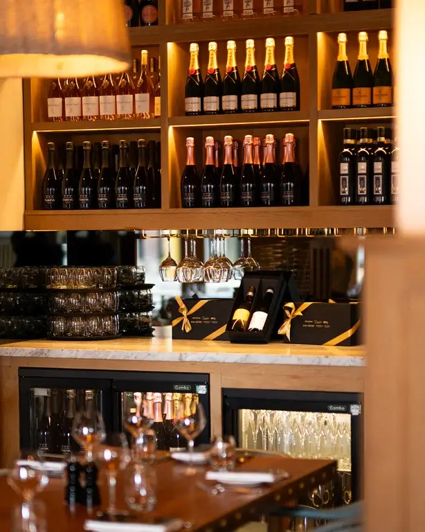 A beautifully arranged bar featuring shelves of champagne bottles, wine glasses, and stylish gift boxes on a marble counter.