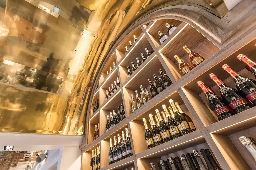 Elegant display of various champagne bottles on wooden shelves, set against a reflective gold ceiling in a sophisticated setting.