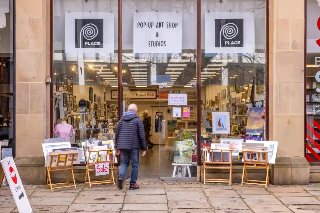 An art shop entrance displays various paintings outside, with a welcoming sign for browsers and people entering the gallery.