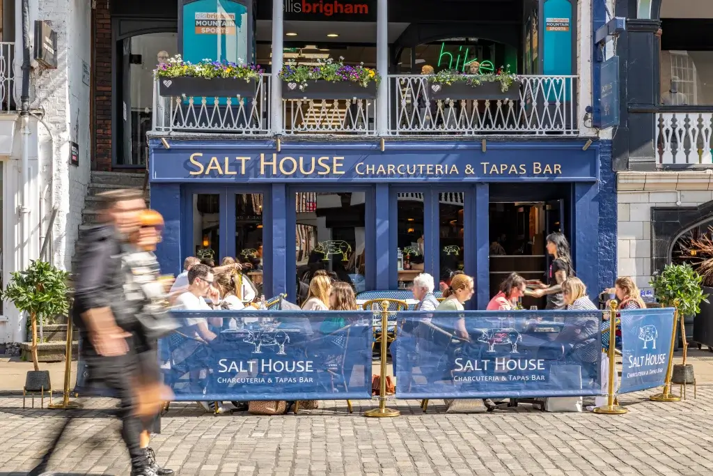 A bustling charcuterie and tapas bar named Salt House, with outdoor seating and patrons enjoying their meals on a sunny day.
