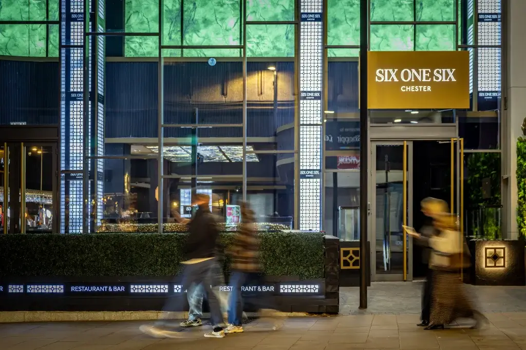 A modern restaurant entrance, "Six One Six" in Chester, features stylish signage and patrons blurred while walking by.