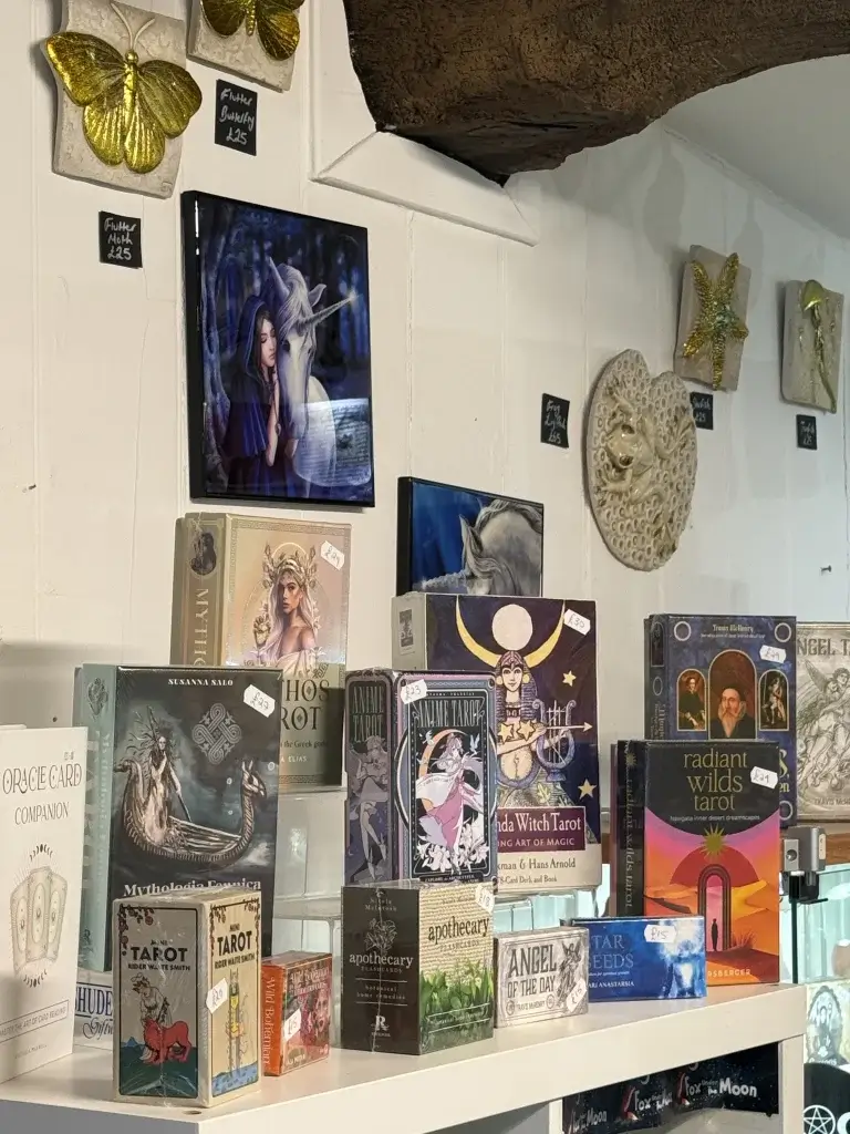 A display of various tarot card decks and decorative items, including golden butterflies and mythical artwork, on a white shelf.