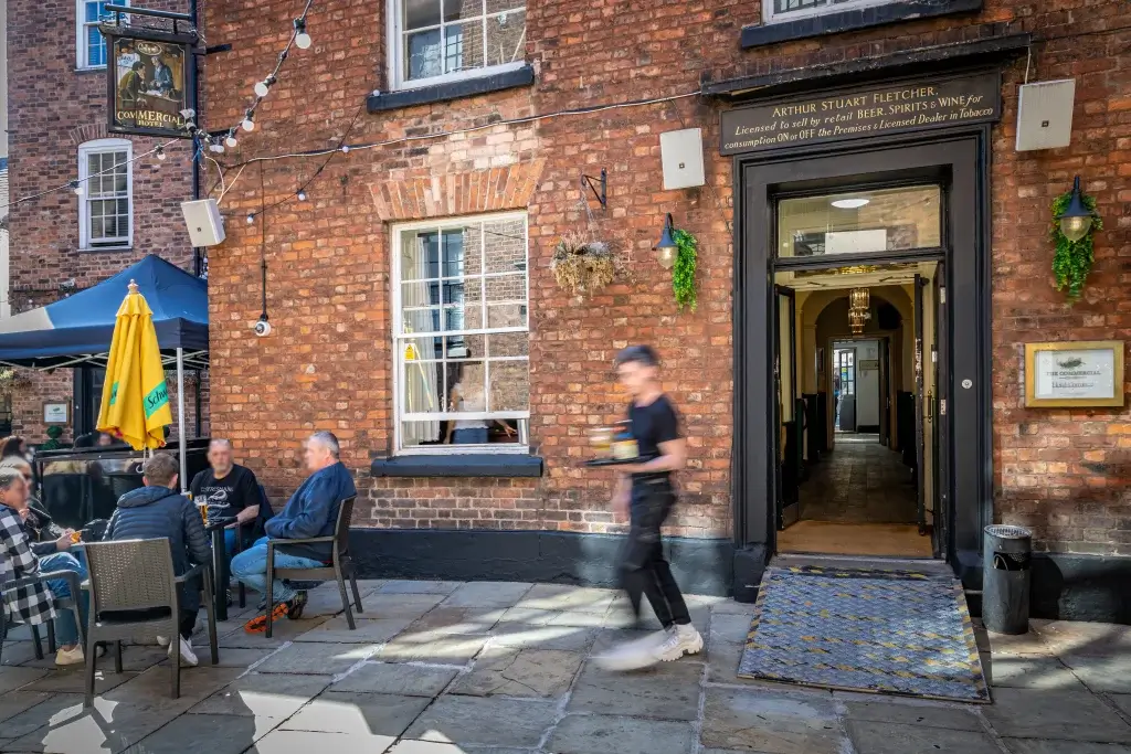 A bustling outdoor seating area with patrons enjoying drinks, surrounded by brick walls and festive string lights.