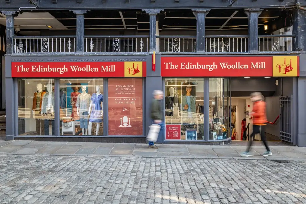 A storefront of The Edinburgh Woollen Mill featuring mannequins dressed in clothing and a sign displaying cashmere scarf promotions.