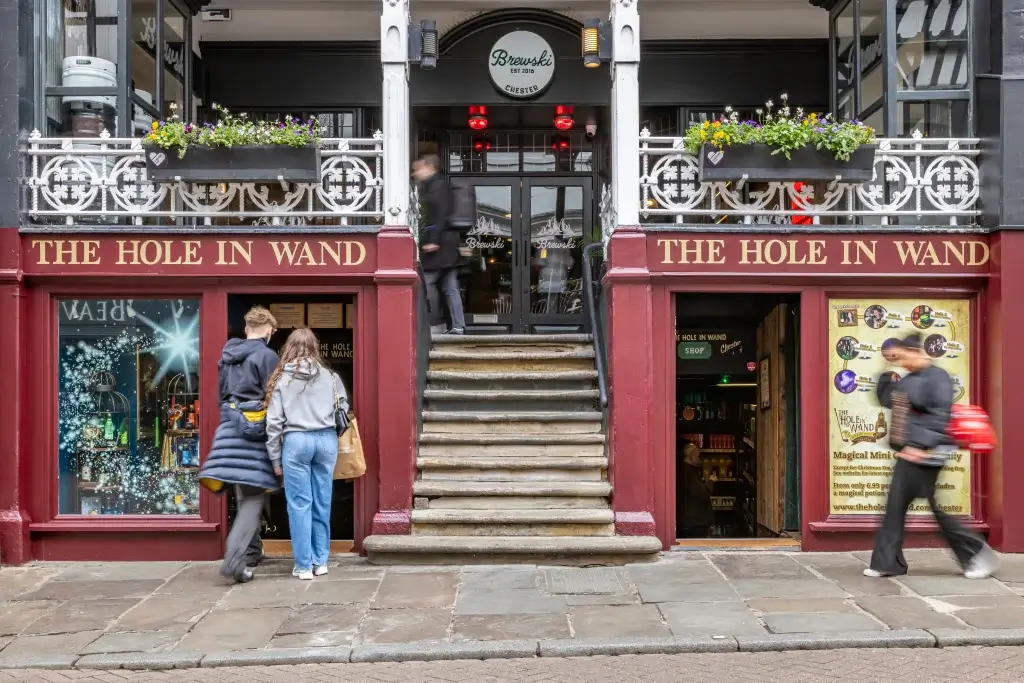A couple approaches the entrance of "The Hole in Wand," a charming shop featuring magical decor and a window display with sparkling effects.