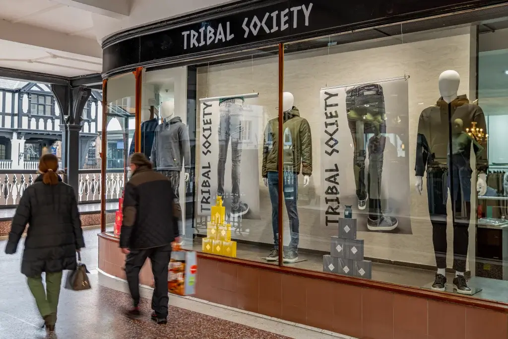A storefront displays mannequins in trendy clothing, with two shoppers walking by, showcasing the "Tribal Society" brand.
