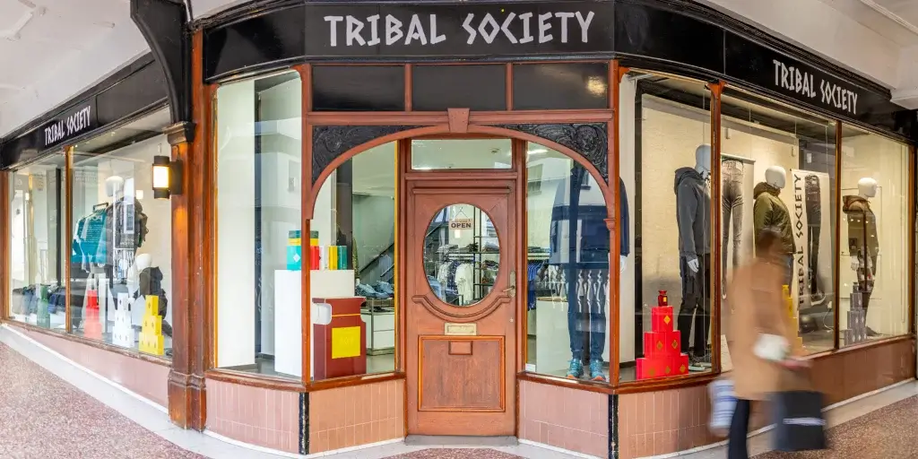 A woman walks past the storefront of Tribal Society, showcasing colorful clothing and a welcoming "OPEN" sign.