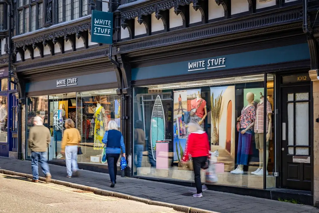Three people walk past the "White Stuff" store, showcasing vibrant clothing and accessories in the display window.
