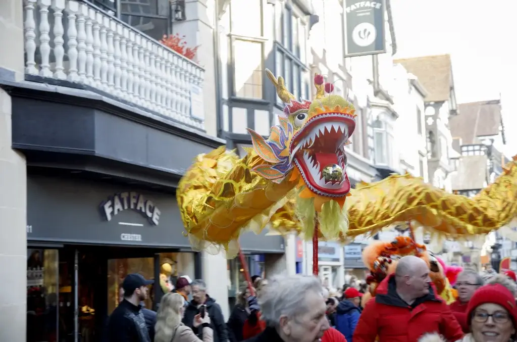 A Lunar New Year performance of people holding up a yellow dragon sculpture in front of a shop