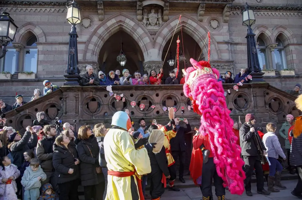 A Lunar New Year performance of people holding up a pink dragon in front of a crowd of people in front of a historic building