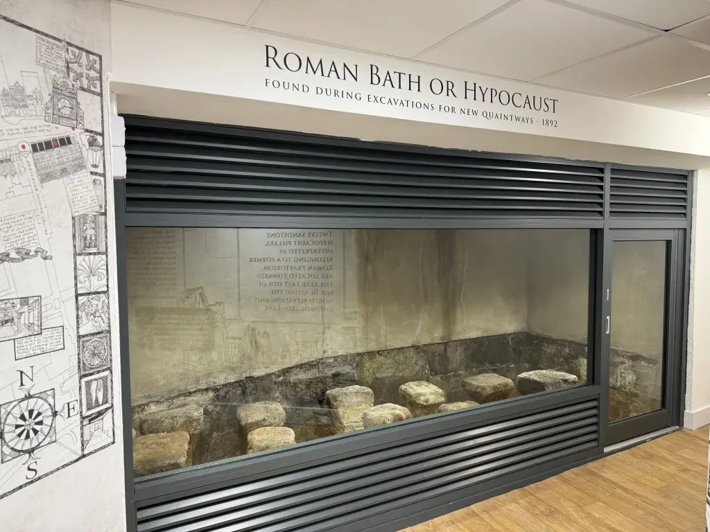Display of a Roman bath or hypocaust, discovered in 1892, with stone supports visible behind protective glass.
