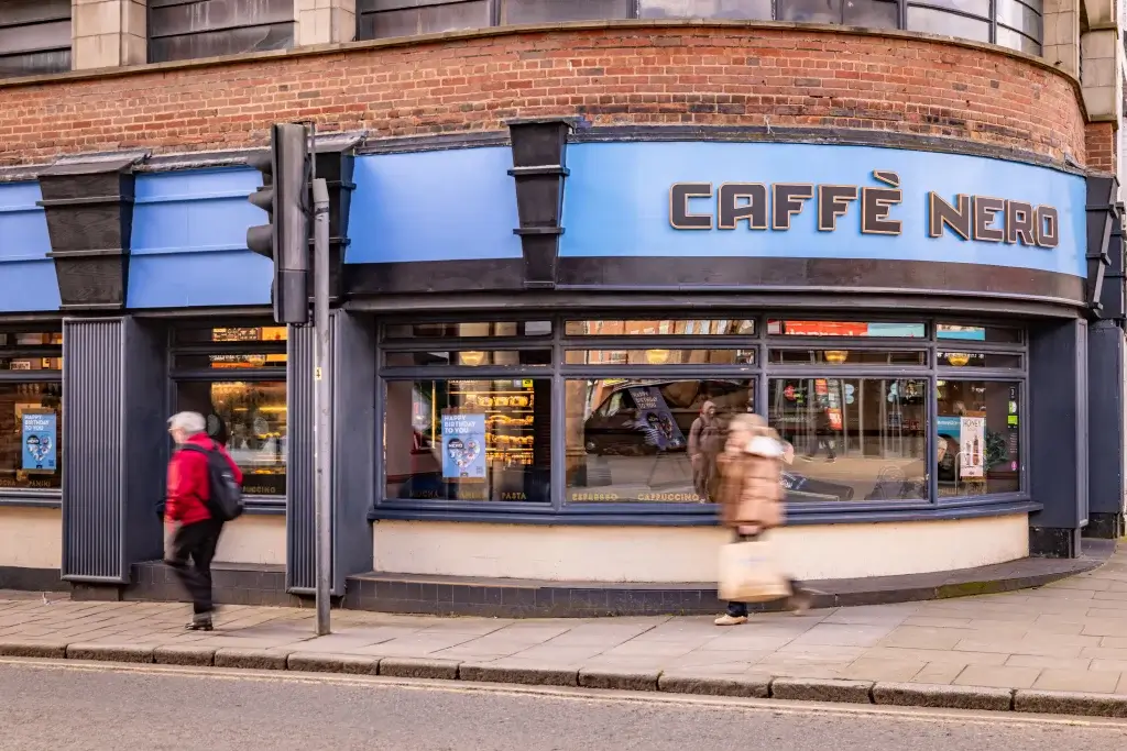 a art deco shopfront with blue and black painted wood and curved window, people walking past outside and words Caffè Nero displayed above