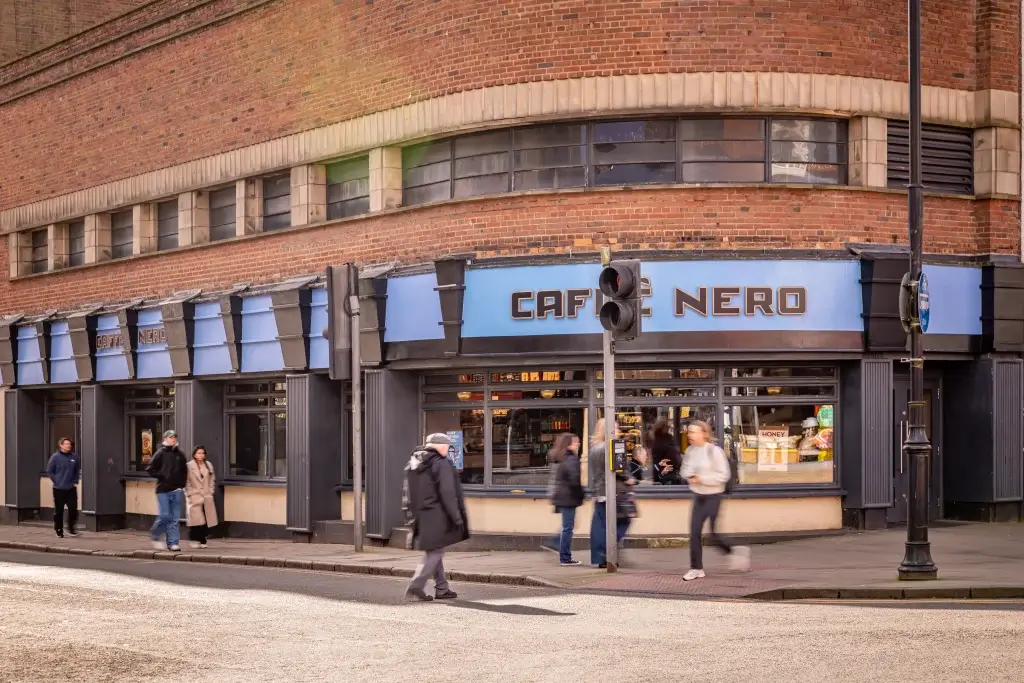 a art deco shopfront with blue and black painted wood and curved window, people walking past outside and words Caffè Nero displayed above