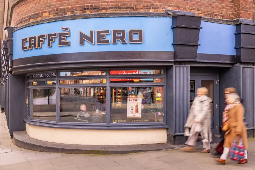 a art deco shopfront with blue and black painted wood and curved window, people walking past outside and words Caffè Nero displayed above