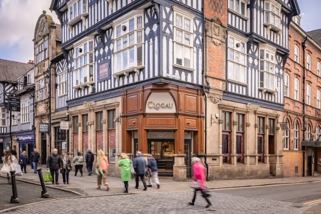 A busy street scene featuring the Clogau jewelry store in a historic, half-timbered building, with pedestrians walking by.