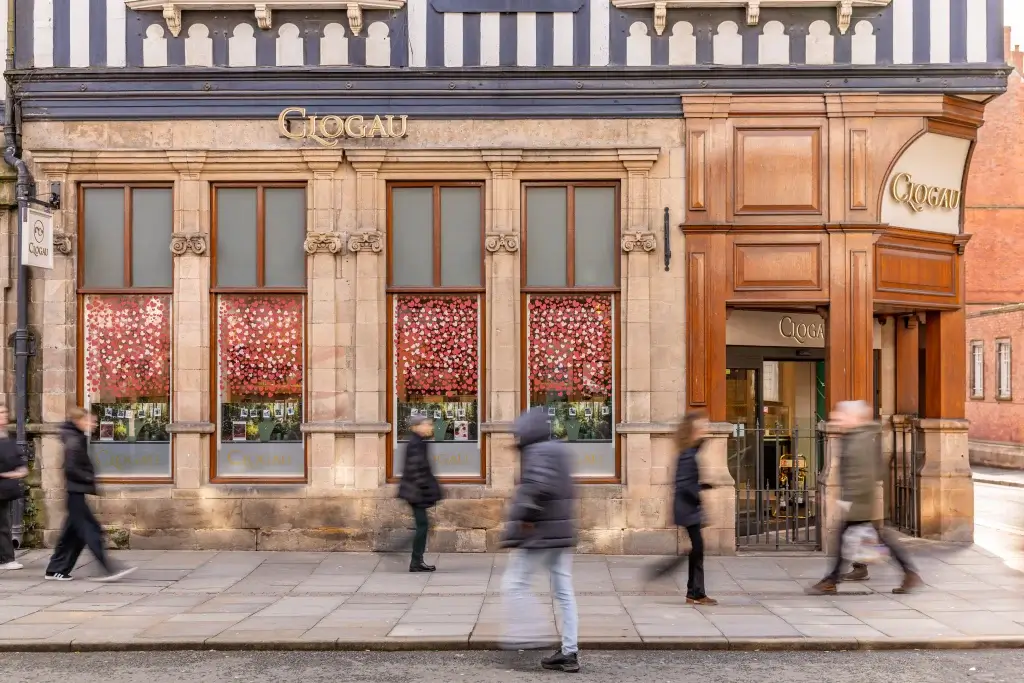 Historic shop front of Clogau, featuring floral window displays, with pedestrians walking by on a bustling street.