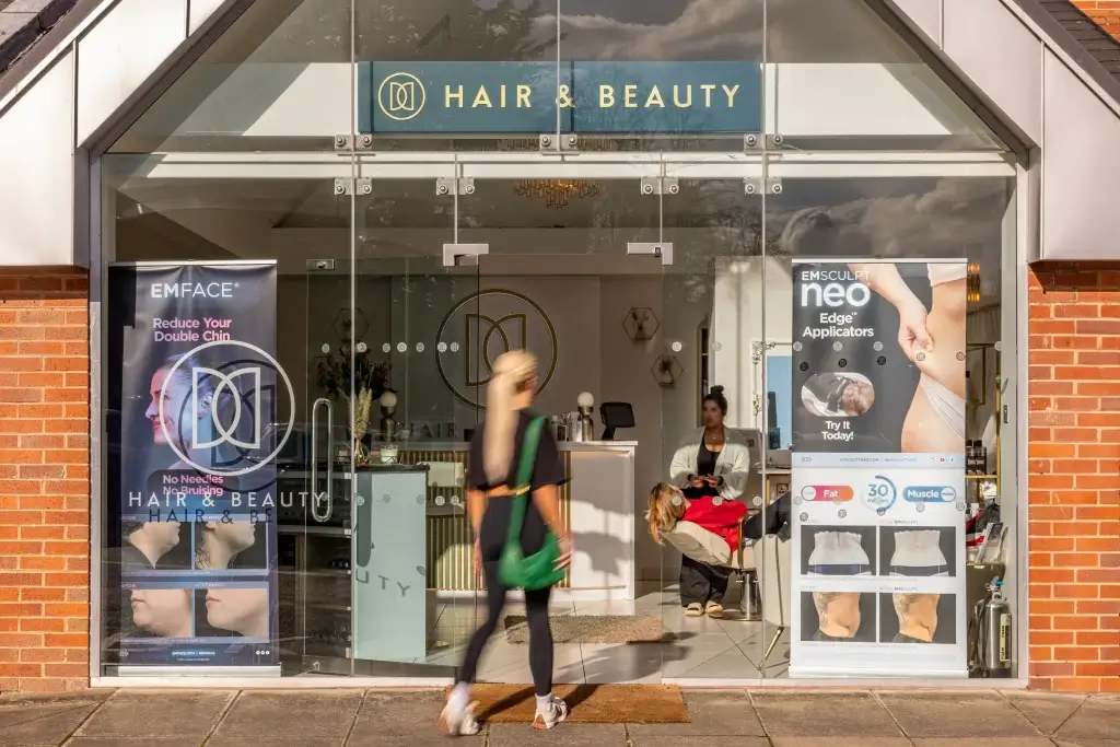 A stylish hair and beauty salon entrance, featuring banners advertising treatments and a welcoming interior with clients and staff visible.