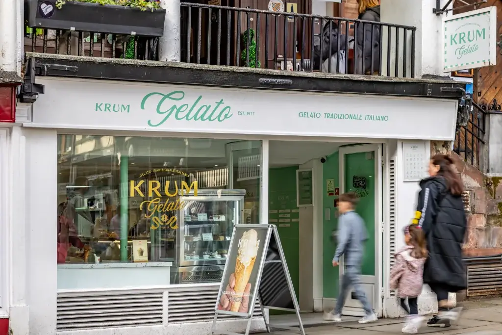 A quaint gelato shop named "Krum Gelato" features a welcoming storefront and customers enjoying their time on the street.