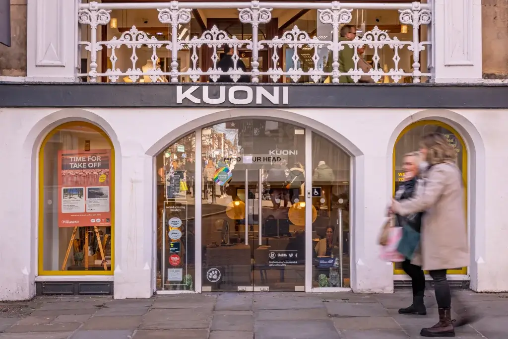 Exterior view of a Kuoni travel agency, featuring large arched windows, a welcoming entrance, and people walking by on a busy street.