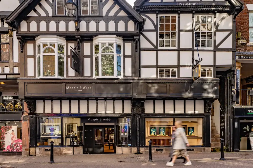 A historical black-and-white timbered building features a jewelry store, Mappin & Webb, with a pedestrian walking by.