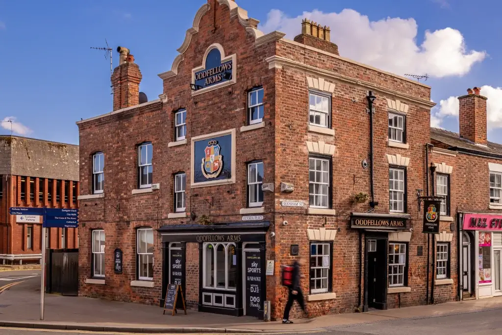 Historic Oddfellows Arms pub with red brick exterior, featuring a colorful sign, street signs, and a pedestrian walking by.