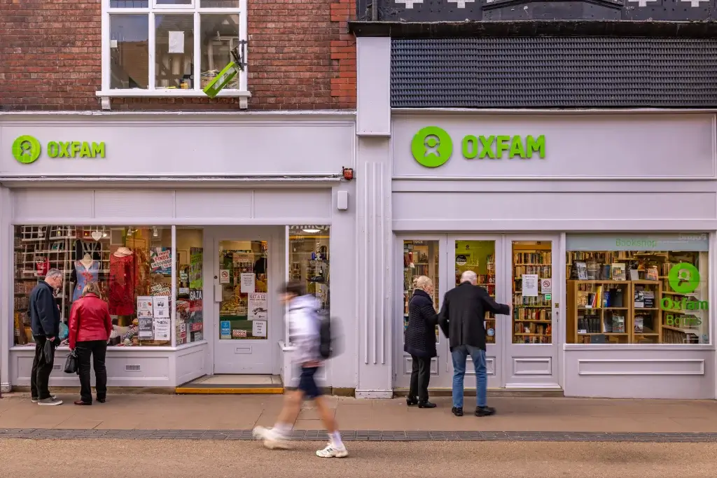 Exterior view of an Oxfam shop with customers browsing, showcasing books and various items in the windows.