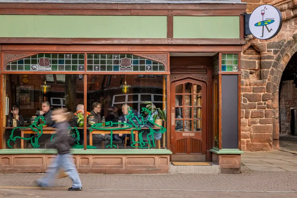 A bustling café with wooden decor and green accents, featuring seated patrons and playful dog illustrations on the windows.
