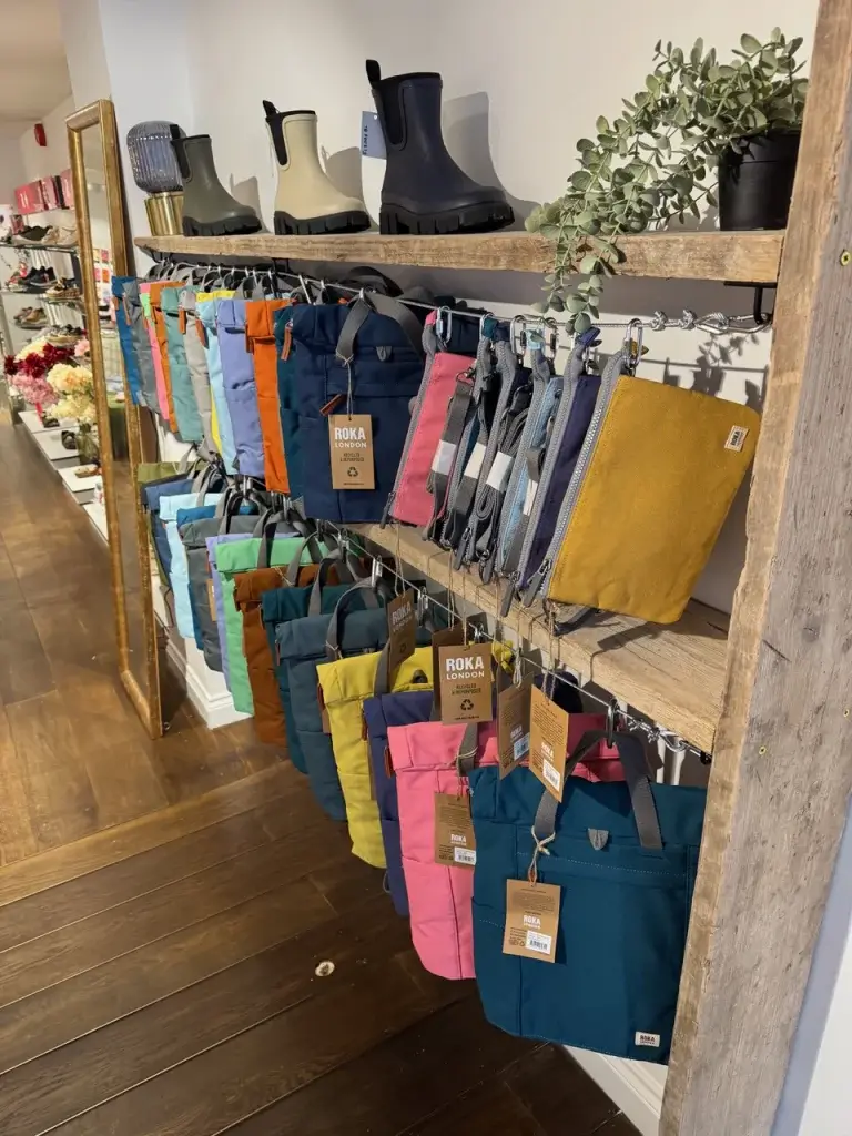 A display of colorful bags on wooden shelves, featuring various styles and sizes, alongside stylish rain boots and decorative plants.