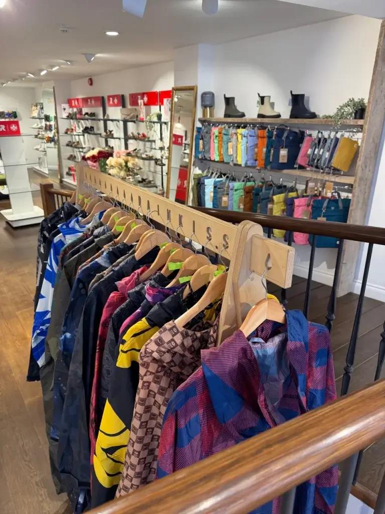 Colorful clothing hangs on wooden racks in a stylish boutique, with additional garments displayed on shelves in the background.